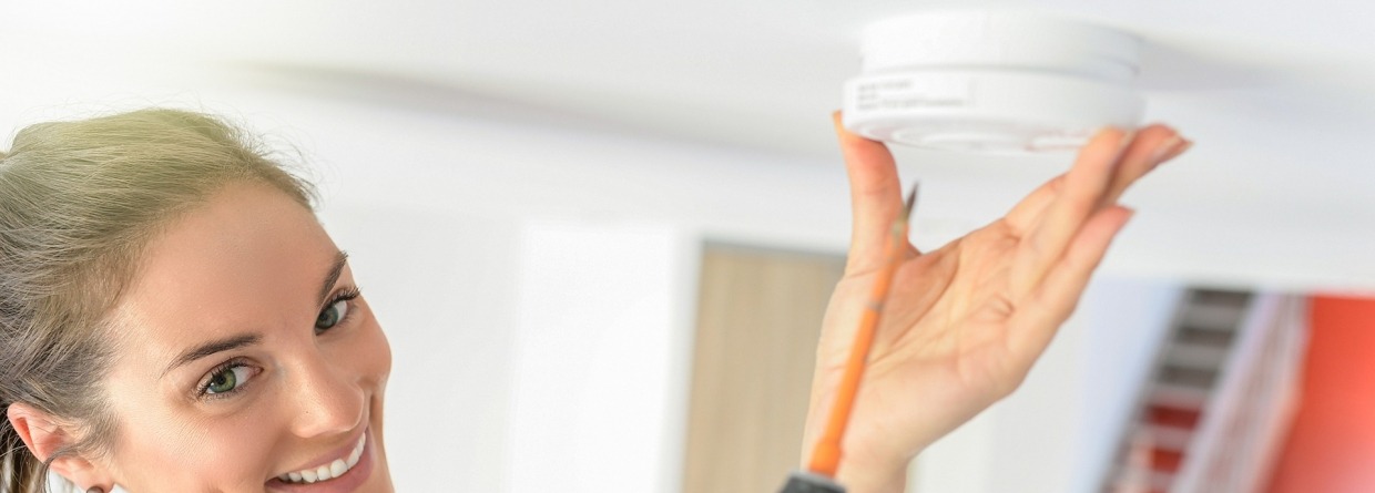 Jonge vrouw hangt rookmelder aan plafond