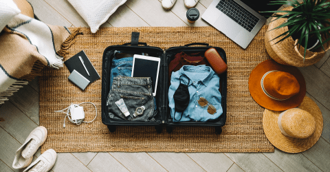 Campagne vakantiegevoel; koffer met kleding, schoenen, hoeden en digitale apparatuur uitgestald op de grond