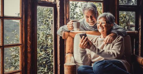 Een paar twee oude en volwassen mensen die thuis samen de telefoon gebruiken op de bank.